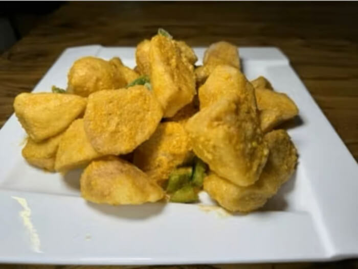 Crispy, golden-battered eggplant cubes stacked on a plate with savory duck yolk coating.