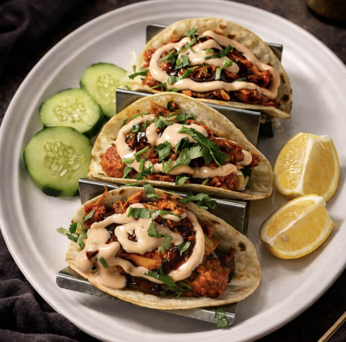 Soft tacos filled with creamy butter chicken, garnished with fresh herbs and sauce.