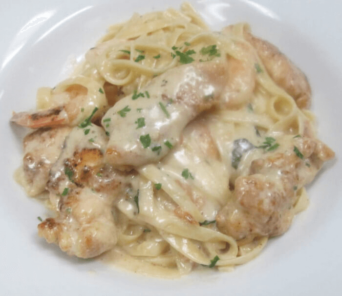 Creamy Alfredo fettuccine pasta with grilled chicken slices, garnished with parsley and fresh parmesan cheese on a white plate.