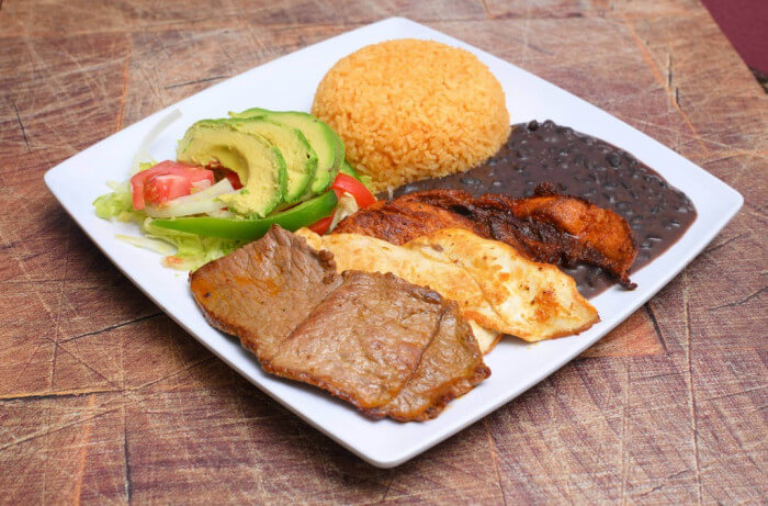 Hearty Tex-Mex trio meat platter featuring grilled chicken, spicy pork, and tender steak, served with Mexican rice, refried beans, and a fresh salad topped with creamy avocado slices.