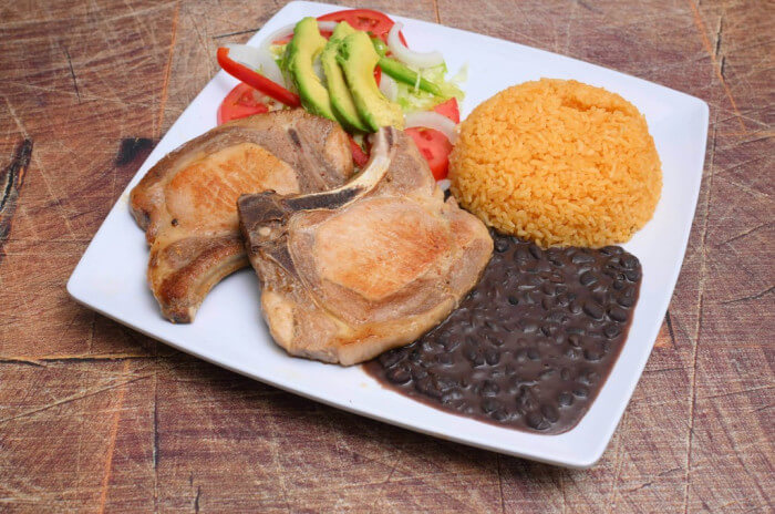 Perth Amboy grilled pork chop plate with rice, beans, and avocado salad.