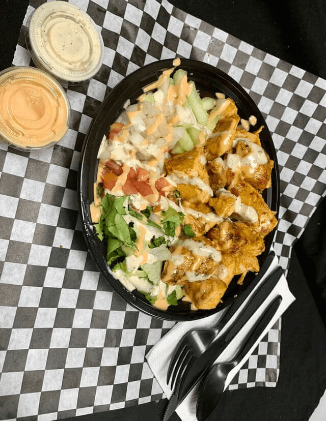 Seasoned Halal chicken on rice with tomatoes, cucumbers, onions, and sauces.