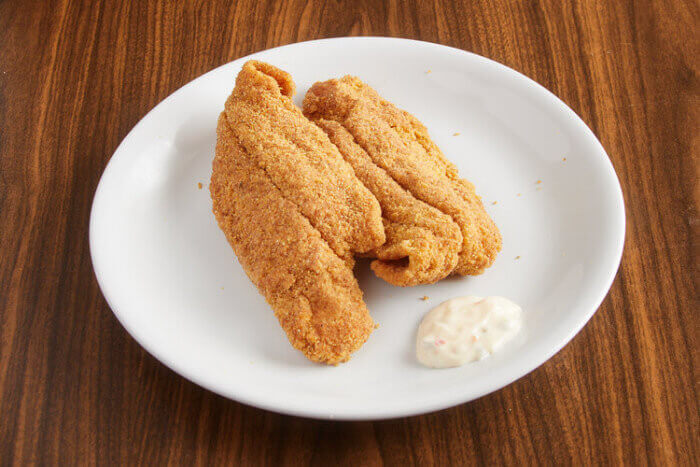 Fried catfish fillets with traditional sides and lemon wedges.