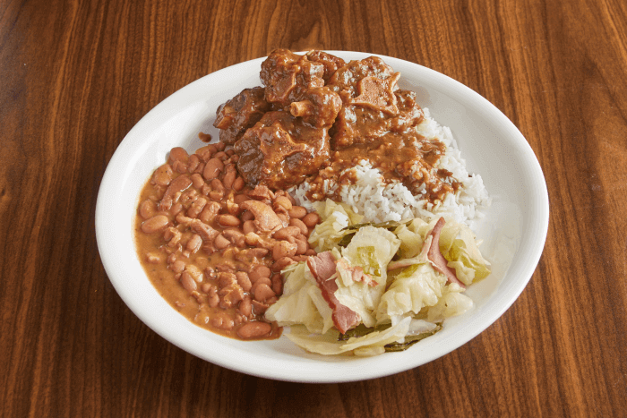 Plate of oxtails with collards, sweet potatoes, and cornbread.