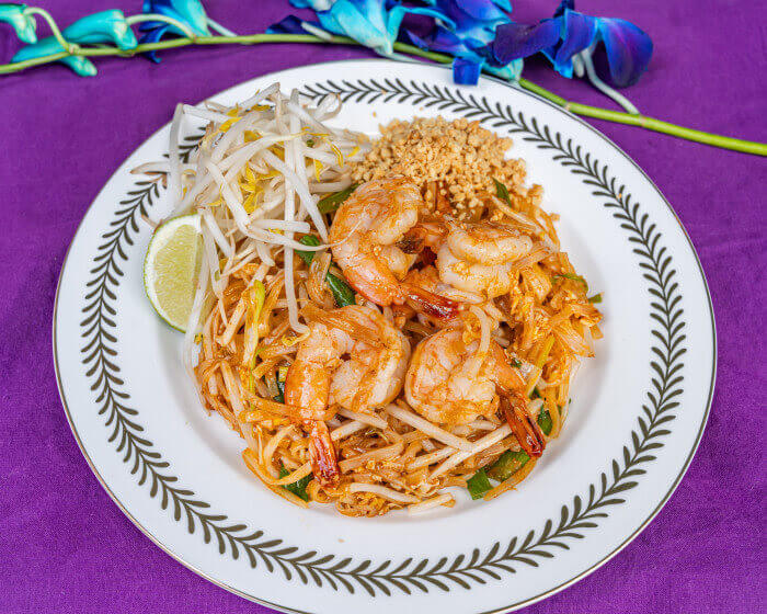 Stir-fried thin rice noodles with shrimp, egg, scallions, bean sprouts, and crushed peanuts, garnished with lime and cilantro.