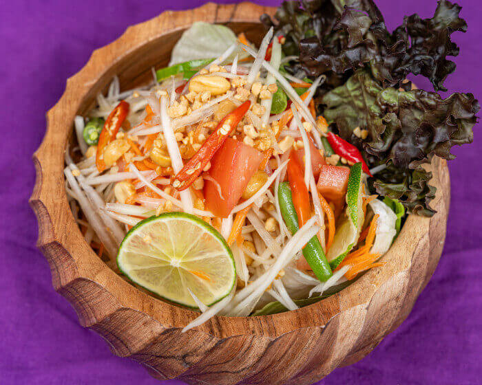 Fresh papaya salad with shredded green papaya, cherry tomatoes, long beans, and roasted peanuts drizzled with lime dressing.