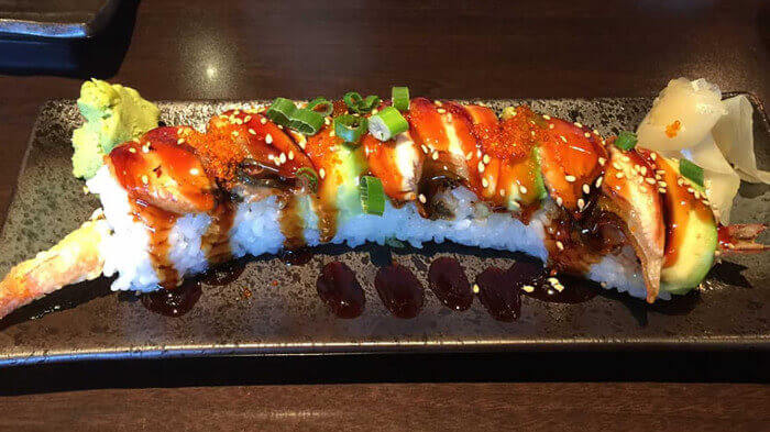 Sushi roll topped with BBQ eel, avocado, fish roe, and sesame on a black slate plate