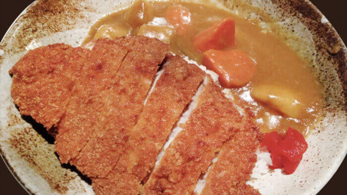 Japanese pork katsu curry over rice with pickled vegetables on the side