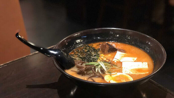Spicy ramen bowl with pork, tofu, egg, corn, and green onions in a creamy broth
