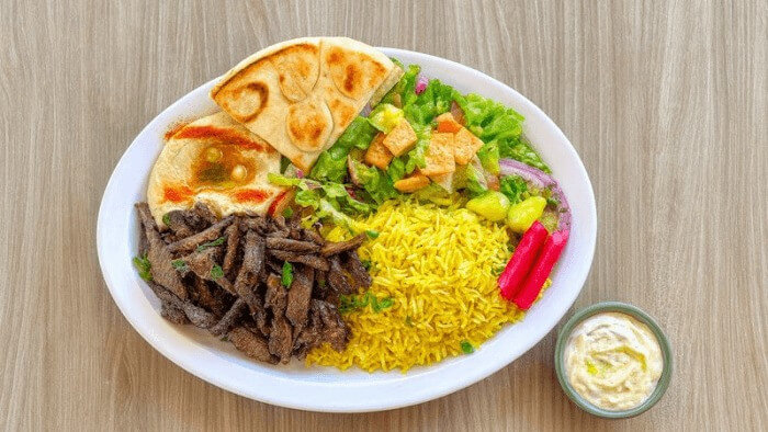 Beef shawarma with seasoned rice, dip, salad, and grilled pita.