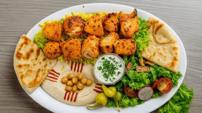 Two skewers of chicken tender kabob with rice, hummus, salad, and pita.