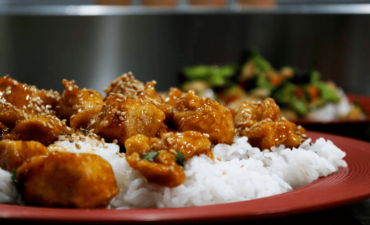 Red plate of teriyaki chicken on top of steamed white rice