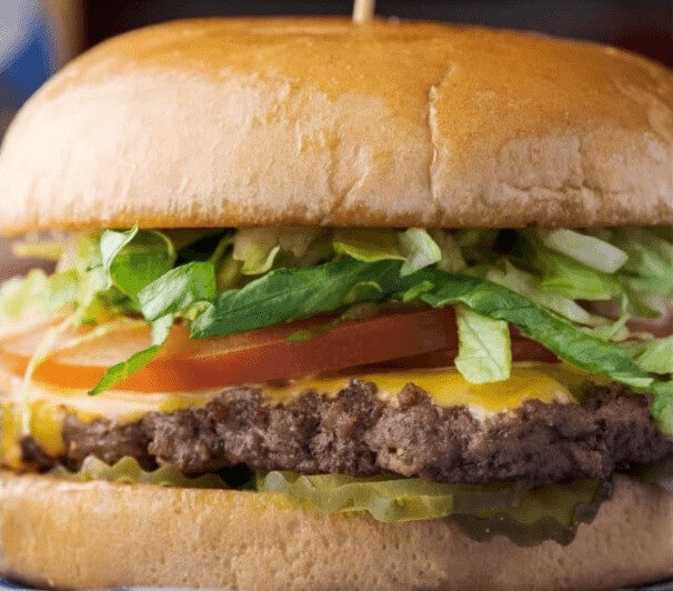Classic American burger topped with mayo, mustard, lettuce, tomato, onions, and pickles on a toasted bun.