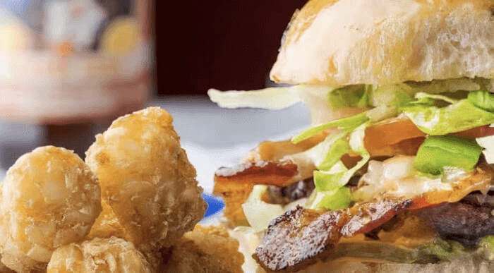 Signature burger on a jalapeño sourdough bun, with crispy bacon, guacamole, pepper jack cheese, grilled onions, bell peppers, lettuce, tomato, and pickles.